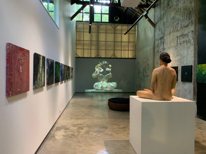 A person sitting on a pedestal in a room with art on the wall

Description automatically generated